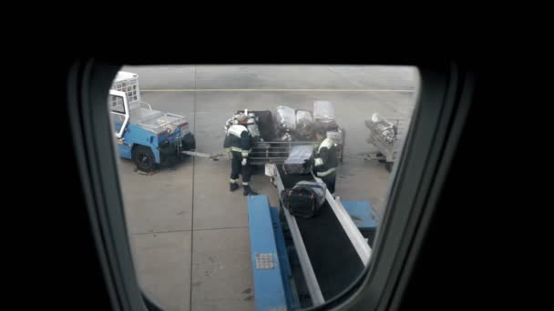 BORISPOL, UKRAINE, OCTOBER 30, 2020: працівники аеропорту розвантажують сумки, валізи, багаж пасажирів з багажного відділення літака. Вид з ілюмінатора, вікно літака. прибуття — стокове відео