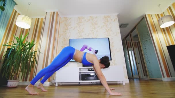 Online fitness training op afstand, thuis. Jonge vrouw, in sportkleding, kijken naar tutorial video met fitnesscoach op tv en thuis oefenen. Online workout. — Stockvideo