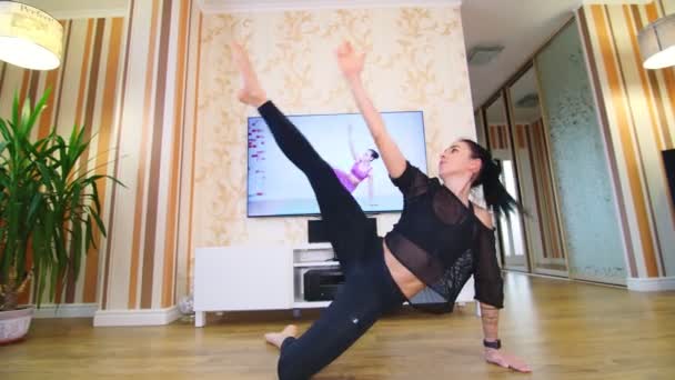 Online workout, remotely. Young woman, in sportswear, watching tutorial video with fitness coach on TV and practicing exercises at home. doing sports during lockdown, at home — Stock Video