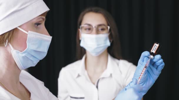 Coronavirus vaccinatie. verpleegkundige of arts trekt met beschermend masker en medische handschoenen vloeibaar vaccin uit glazen reageerbuisfles in een injectiespuit voor covid-19 vaccinatie. — Stockvideo