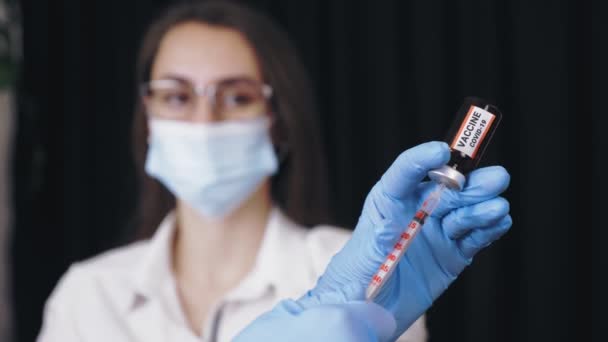 Coronavirus vaccinatie. close-up, handen van verpleegkundige of arts, in blauwe medische handschoenen, zuig vloeibaar vaccin uit glazen reageerbuisfles op in een spuit voor covid-19 vaccinatie. — Stockvideo