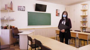 Uzaktan eğitim, okullarda tecrit. Koruyucu maskeli bir kadın öğretmen, elinde dizüstü bilgisayarla boş bir okul sınıfında duruyor. Koronavirüs yüzünden tam tecrit..
