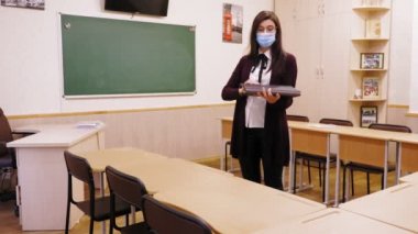 Uzaktan eğitim, okullarda tecrit. Koruyucu maskeli bir kadın öğretmen, elinde dizüstü bilgisayarla boş bir okul sınıfında duruyor. Koronavirüs yüzünden tam tecrit..
