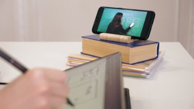 Uzaktan öğrenme, online eğitim. Akıllı telefon ekranına yakın çekim. Liseli kız çevrimiçi video dersi izliyor ve tablete notlar alıyor. Evde online ders çalışıyorum..