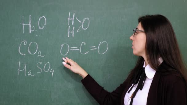Online schooling. Female teacher is holding online chemistry lesson. She is writing formulas with chalk on blackboard, in school class. remote teaching. live video streaming from class. — Stock Video