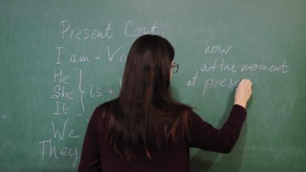 オンライン教育。女性教師がオンライン英語レッスンを行っています。彼女は黒板にチョークで文法規則を書いている。遠隔教育だ。授業中の生ビデオストリーミング. — ストック動画