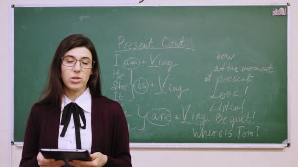 Διαδικτυακή εκπαίδευση. Γυναίκα δάσκαλος κατέχει online μάθημα αγγλικών στην τάξη του σχολείου. φόντο μαυροπίνακα με γραπτούς κανόνες γραμματικής σε αυτό. εξ αποστάσεως διδασκαλία. ζωντανή ροή βίντεο από την τάξη. — Αρχείο Βίντεο