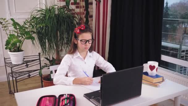 Afstandsonderwijs, online onderwijs. schoolmeisje kijken online tutorial video les op laptop en het maken van notities in copybook. thuis online studeren. — Stockvideo