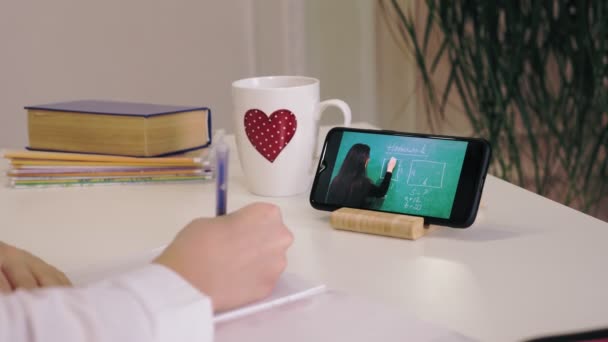 Enseignement à distance, enseignement en ligne. gros plan de l'écran du smartphone. écolière regarder leçon vidéo tutoriel en ligne et de prendre des notes dans le livre. étudier en ligne à la maison. — Video