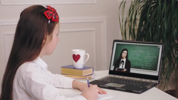 Enseignement à distance, enseignement en ligne. écolière regarder tutoriel en ligne leçon vidéo avec les enseignants explications sur l'écran de l'ordinateur portable et de prendre des notes dans le copybook. étudier en ligne à la maison. — Video