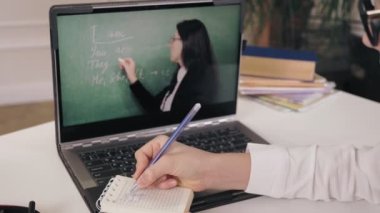 Uzaktan öğrenme, online eğitim. Laptop ekranına yakın çekim. Liseli kız çevrimiçi video dersi izliyor ve not defterine not alıyor. Evde online ders çalışıyorum..