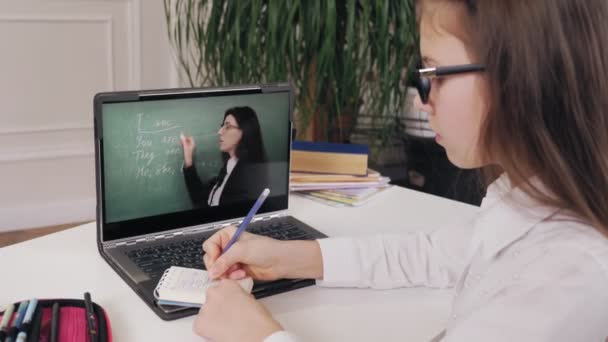 Дистанційне навчання, онлайн-освіта. школярка дивиться онлайн відео урок з поясненнями вчителів на екрані ноутбука і робить нотатки в блокноті. навчання онлайн вдома . — стокове відео
