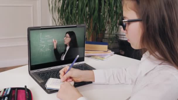 Educación a distancia, educación en línea. colegiala viendo video tutorial en línea lección con los profesores explicaciones en la pantalla del ordenador portátil y tomar notas en el cuaderno. estudiar en línea en casa. — Vídeos de Stock