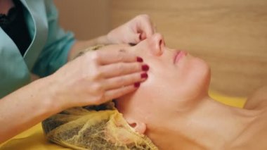 Kozmetoloji, yüz temizleme. Kadınlar için kozmetik prosedürler. Yakın plan. Kadın kanepede uzanıyor ve güzellik kliniğinde yüz temizleme ameliyatı oluyor. Cilt bakımı, cilt bakımı.