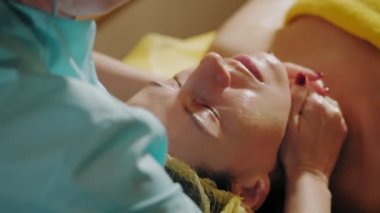 Yaşlanma önleyici prosedür, yüz masajı. Yakın plan. Kadın kanepede uzanıyor ve yüz masajı yaptırıyor. Güzellik kliniğinde yüz ve yüz derisi kanalizasyonu için. Cilt bakımı, kozmetoloji
