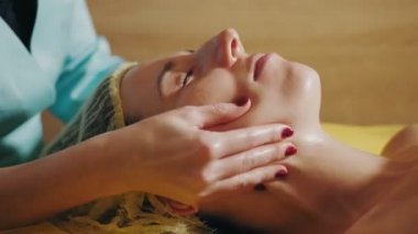 Yaşlanma önleyici prosedür, yüz masajı. Yakın plan. Kadın kanepede uzanıyor ve yüz masajı yaptırıyor. Güzellik kliniğinde yüz ve yüz derisi kanalizasyonu için. Cilt bakımı, kozmetoloji
