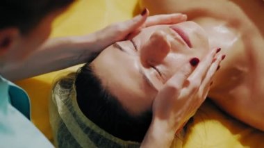 Yaşlanma önleyici prosedür, yüz masajı. Yakın plan. Kadın kanepede uzanıyor ve yüz masajı yaptırıyor. Güzellik kliniğinde yüz ve yüz derisi kanalizasyonu için. Cilt bakımı, kozmetoloji