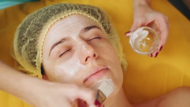 Kosmetologi ansiktsmask. närbild. kvinna ligger på soffan och få ansiktsbehandling hudvård förfarande, på skönhetskliniken. Hudvård, dermatologisk behandling. — Stockvideo