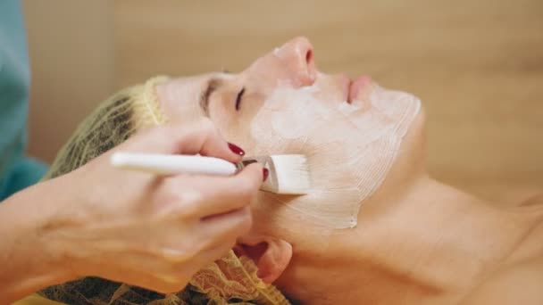 Máscara facial de cosmetología. Primer plano. mujer está acostada en el sofá y obtener el procedimiento de cuidado de la piel facial, en la clínica de belleza. Cuidado de la piel, tratamiento dermatológico. — Vídeos de Stock