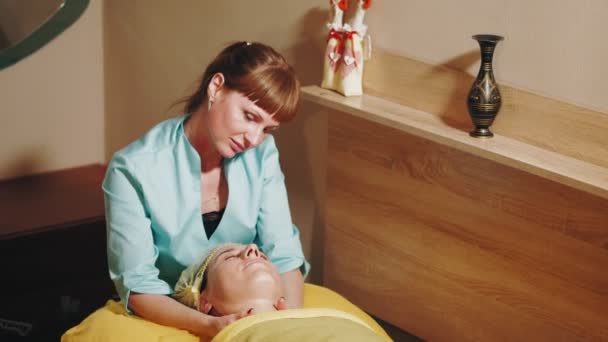 Kosmetologia przeciwstarzeniowa. masaż twarzy. kobieta dostaje masaż twarzy i dekolt do tonizacji mięśni i drenażu limfatycznego skóry twarzy, w klinice kosmetycznej. Pielęgnacja skóry, zabiegi kosmetyczne — Wideo stockowe