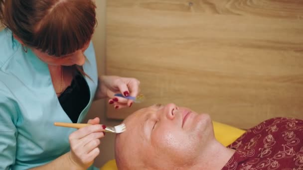 Kozmetika, férfi arctisztítás. kozmetikai eljárások férfiaknak. A férfi a kanapén fekszik és arcbőrápoló kezelésen van a szépségklinikán. Bőrápolás bőrgyógyászati kezelése. — Stock videók