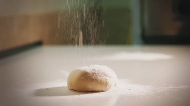Yemek pişirme, fırın. Yakın plan. Şef fırında pişirmek için un serpiyor, masanın üzerinde duruyor. Mutfak masasında un içinde bir parça pizza hamuru yatıyor.