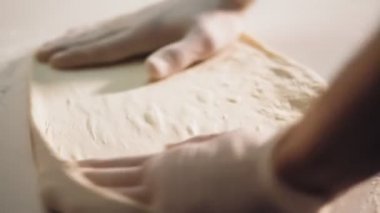 Yemek pişirme, fırın. Yakın plan. Şef, un serpiştirilmiş pizza hamurunu boş bir şekilde un masasına serper. Şef fırıncı elleri koruyucu eldiven giymiş..