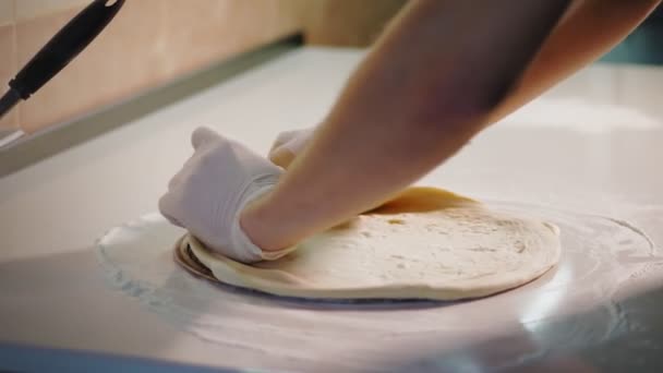 Cooking, bakery . close-up. the chef rolls out pizza dough blank on the sprinkled with flour table . chef baker hands are in protective gloves. — Stock Video