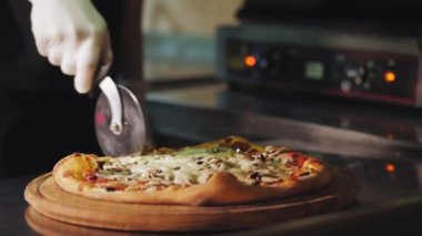 Aşçılık. Pizza yapmak. Yakın plan, şef yeni hazırlanmış sıcak pizzayı özel bir pizza bıçağıyla parçalara ayırıyor. İtalyan pizzası pişirme süreci .