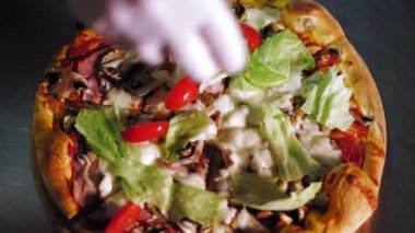 Aşçılık. Pizza yapmak. Yakın çekim, üst görüş. Şef taze pişmiş üzerine dilimlenmiş domatesli sıcak pizza serpiyor. İtalyan pizzası pişirme süreci .