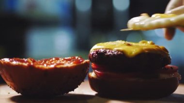 Hamburger pişirmek. Yakın plan. Şef hamburgere lezzetli malzemeler ekler, taze salatalık, domates, sulu, peynirli ızgara biftek ve üstüne kızarmış yumurta gibi. Fast food, abur cubur