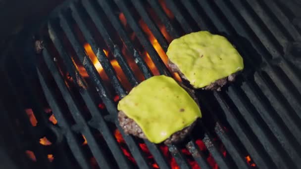 Gotowanie. gotowanie hamburgerów. Zbliżenie. grillowanie świeżego mięsa hamburgery paszteciki z żółtym topionym serem na kozieradki. proces pieczenia medalionów mięsa wołowego na grillu z gorącym płomieniem. fast food, śmieci — Wideo stockowe