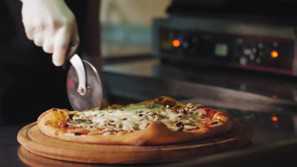 Cucina. A fare la pizza. Primo piano, lo chef taglia una pizza calda appena preparata a pezzi con uno speciale coltello da pizza. processo di cottura della pizza italiana . — Video Stock