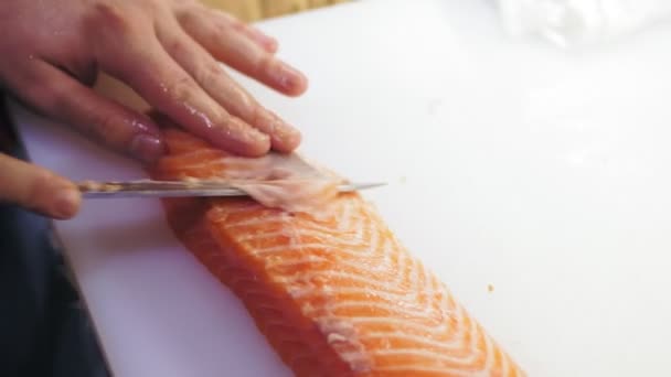 Tradycyjne japońskie jedzenie. Przygotowanie sushi. zbliżenie. Sushi Chef jest cięcie, plastry świeżego łososia filet z nożem na białej desce do krojenia przed przygotowaniem sushi ryb. Przepisy kuchni japońskiej. — Wideo stockowe