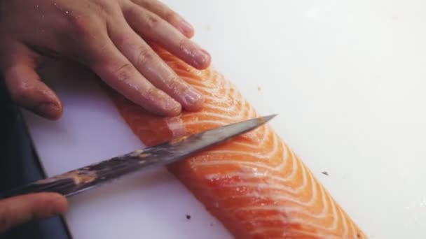Comida tradicional japonesa. Preparación de sushi. Primer plano. Sushi Chef está cortando, cortando filete de salmón fresco con cuchillo en una tabla de cortar blanca antes de preparar sushi de pescado. Recetas de cocina japonesa. — Vídeo de stock