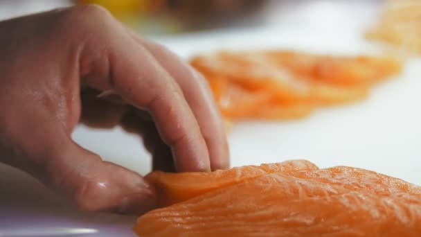 Comida tradicional japonesa. Preparación de sushi. Primer plano. Sushi Chef corta filete de salmón fresco con cuchillo en una tabla de cortar blanca en la barra de sushi. Preparando pescado nigiri de sushi. Recetas de cocina japonesa. — Vídeo de stock