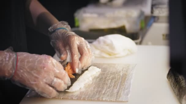 Traditionelles japanisches Essen. Nahaufnahme. Herstellung von Sushi-Rolls in der professionellen Küche einer Sushi-Bar oder eines Restaurants. Hände der Sushi-Köche wickeln das Nori-Laken mit Zutaten. — Stockvideo