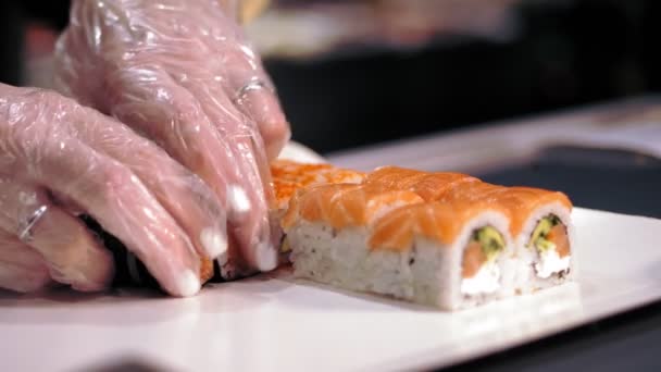 Tradycyjne japońskie jedzenie. zbliżenie. profesjonalny kucharz Sushi wkłada świeżo przygotowane bułki sushi do pudełka na wynos z baru sushi. — Wideo stockowe