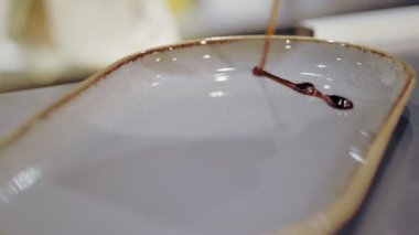 Bir restoranda hizmet etmek. Yakın plan. Şef yemek servisi yapmadan önce boş bir tabağı sos kalıplarıyla süslüyor..