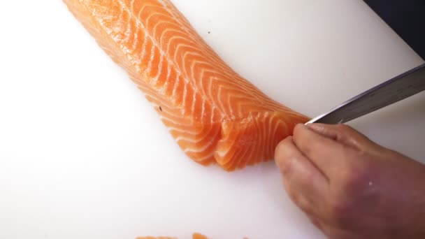 Cuisine traditionnelle japonaise. Préparation des sushis. Gros plan. Sushi Chef tranche un filet de saumon frais avec un couteau sur une planche à découper blanche au bar à sushi. Préparation de sushi nigiri poisson. Recettes de cuisine japonaise. — Video