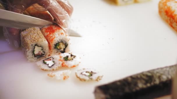 Cuisine traditionnelle japonaise. Gros plan. professionnel Sushi Chef fait des rouleaux de sushi, les couper en morceaux, sur une planche à découper blanche, à la cuisine du bar à sushi. — Video