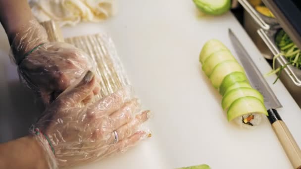 Tradiční japonské jídlo. detailní záběr. Sushi Chefs hands, v jednorázových rukavicích, dělají Sushi Rolls s avokádem v profesionální kuchyni sushi baru nebo restaurace. — Stock video