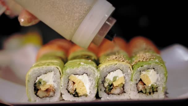 Tradycyjne japońskie jedzenie. zbliżenie. świeżo ugotowane, urozmaicone bułki sushi w pudełku na wynos z baru sushi. szef kuchni posypuje bułki nasionami sezamu — Wideo stockowe