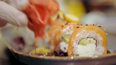 Geleneksel Japon yemekleri. Yakın plan. Suşi şefi taze pişmiş suşi kabını zencefille süslüyor. Japon yemek gurmesi. sanat restoranda hizmet veriyor.