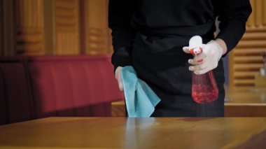 Yakın plan, koruyucu eldivenli bir garson, antiseptik sprey ve temizlik peçetesi kullanarak restoran masalarını siler. pandemik koronavirüs.