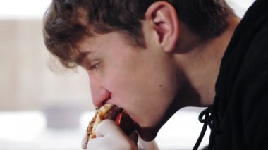 Hamburger yiyorum. Yakından, genç yakışıklı, sulu, lezzetli, yeni hazırlanmış, yağlı burger yiyen, iştahlı bir adam. Fast food, abur cubur.