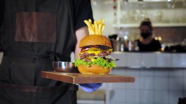 Hamburger, hamburger. Yakın plan. Garson müşteriye sulu, lezzetli, taze hazırlanmış, yağlı bir hamburger ve patates kızartması getiriyor. Fast food, abur cubur.