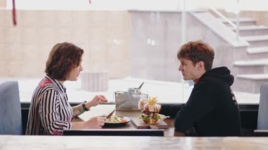 Samimi kafede romantik bir akşam yemeği. Mutlu iki genç, rahat, parlak bir restoranda ya da kafede öğle yemeği yiyor. Genç adam ve kadın gülümsüyor, eğleniyorlar..
