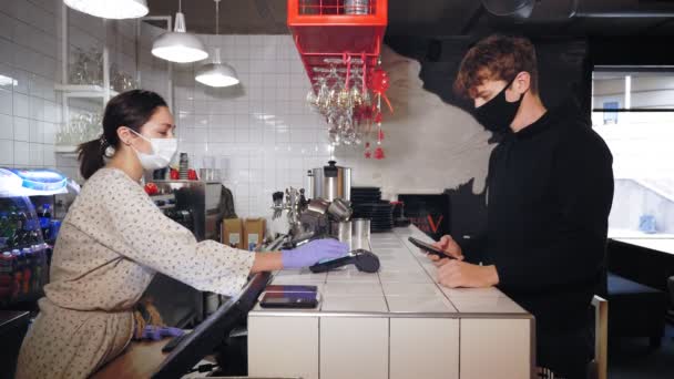 NFC-technologie. serveerster, in beschermend masker en handschoenen, afdrukken bedragen in terminal voor klant contactloze betaling met behulp van smartphone. Mobiel, draadloos betalen. Telefonisch betalen via elektronische betaling — Stockvideo