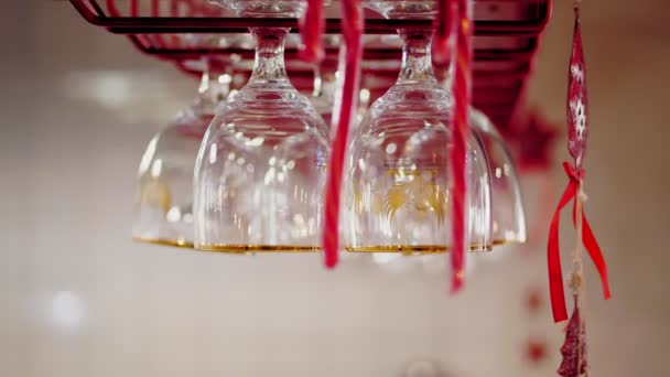 Čisté sklenice u baru. detailní záběr. různé druhy sklenic na nápoje a koktejly visí na speciálních držácích nad barem s vánoční výzdobou — Stock video